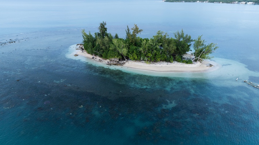 Vista aérea de una pequeña isla con aguas turquesas cristalinas, rodeada por un arrecife de coral.