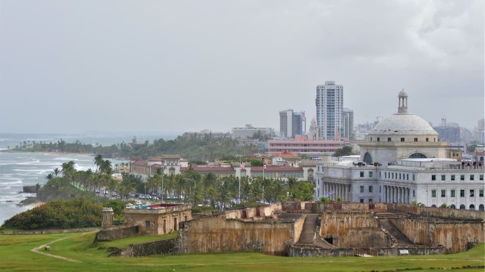 A coastal cityscape with a historic fort, modern buildings, and a beach.