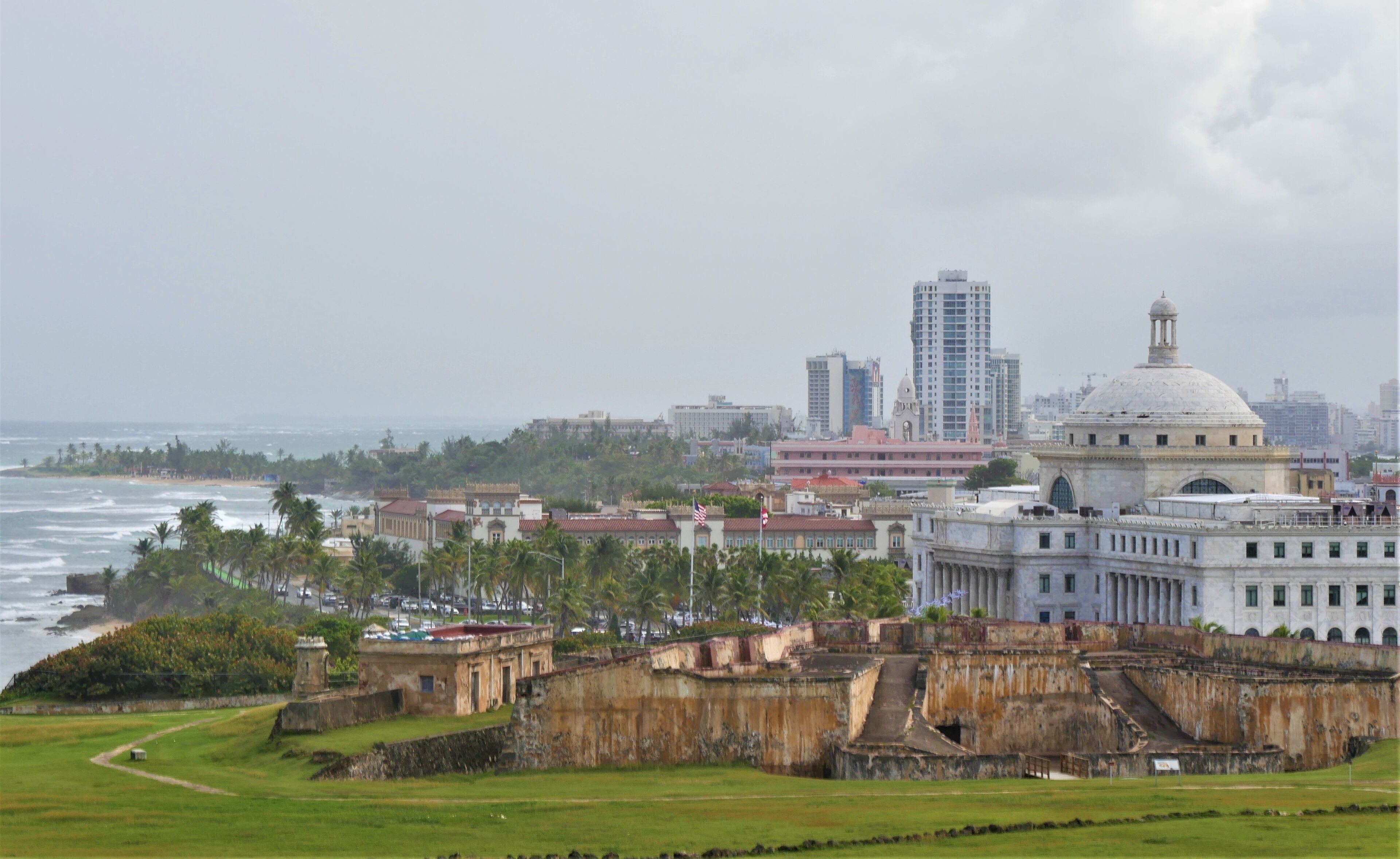A coastal cityscape with a historic fort, modern buildings, and a beach.