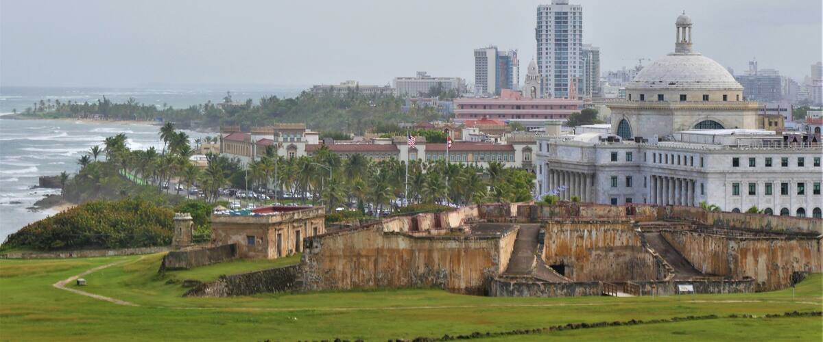 A coastal cityscape with a historic fort, modern buildings, and a beach.
