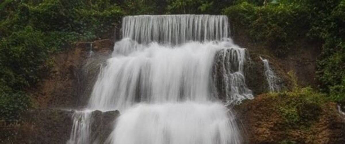 A multi-tiered waterfall cascading down a rocky cliff surrounded by lush greenery.