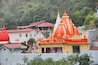 Kainchi Dham Temple, Uttarakhand, where a river flows next to a sacred temple that is surrounded by hills and trees.