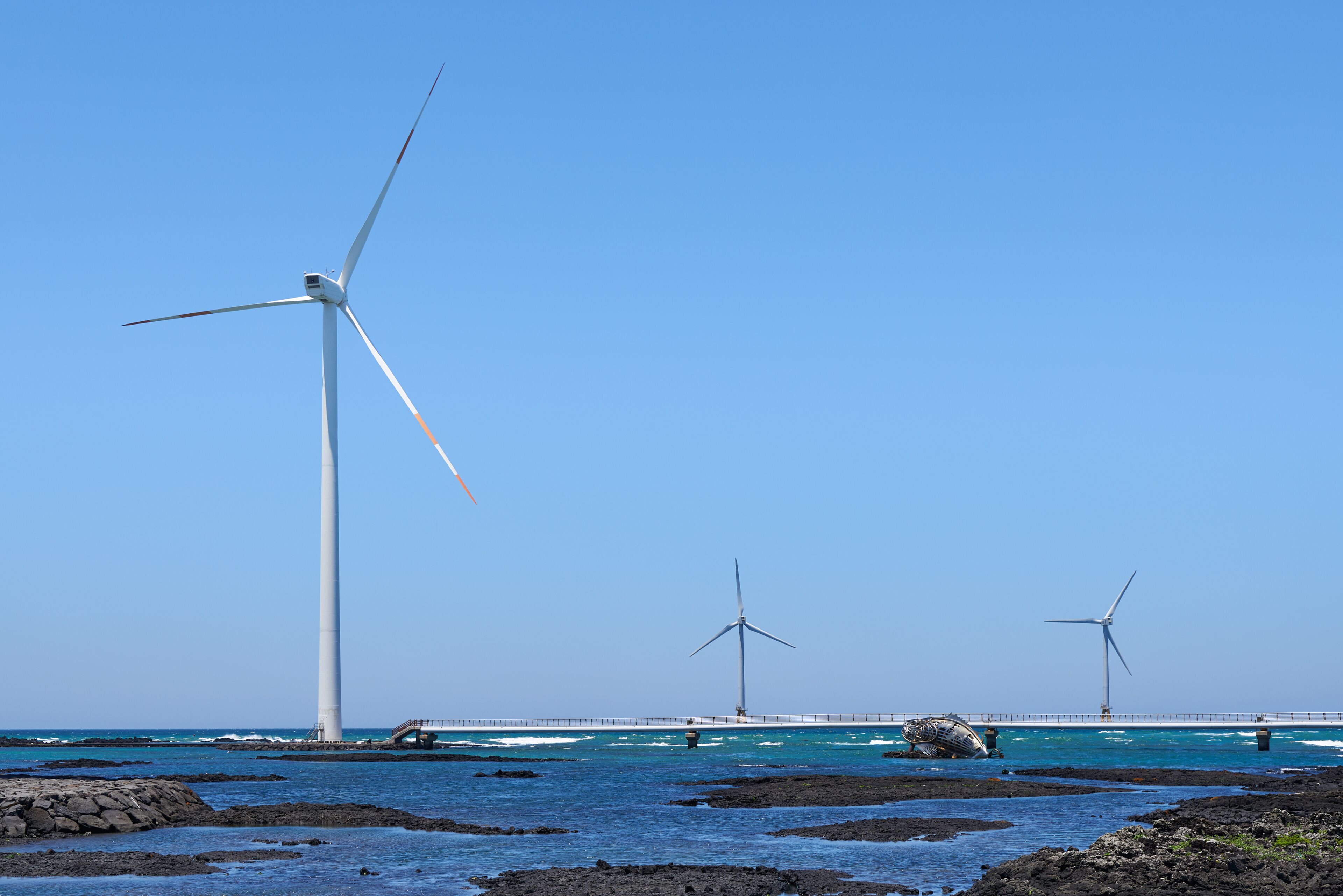 A coastal landscape with three wind turbines and a bridge over the water.
