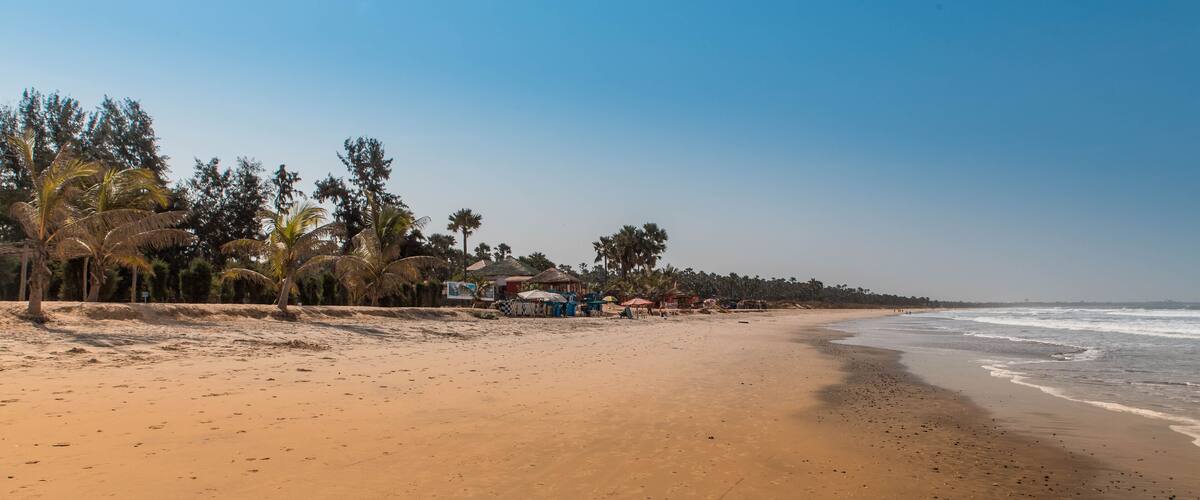 A sandy beach with palm trees and beach huts along the shore.