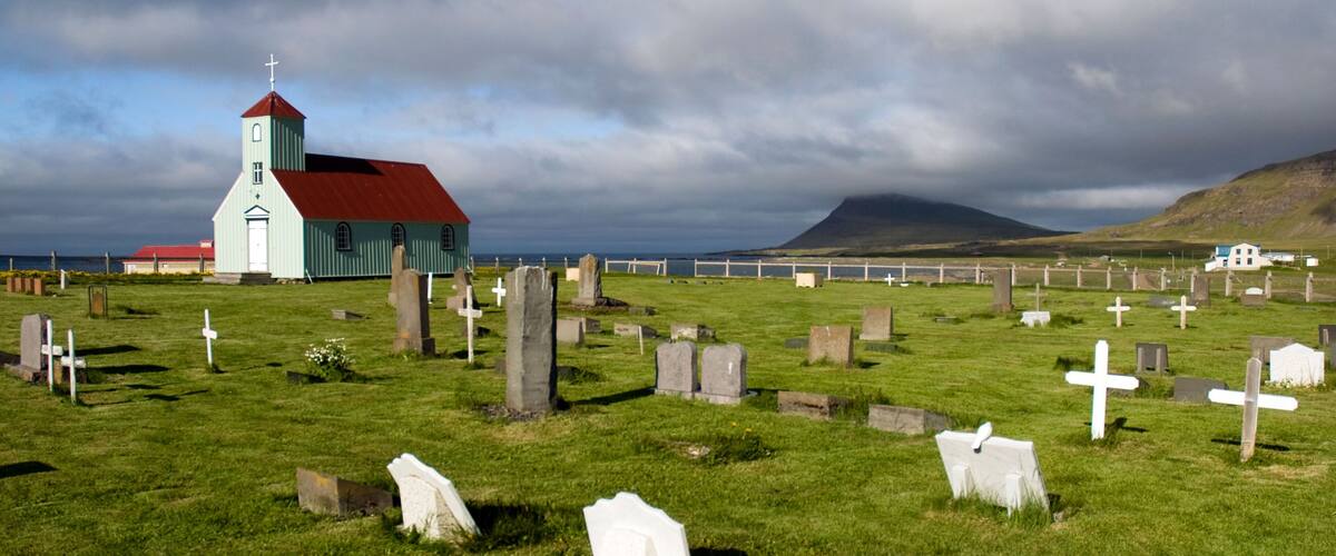 A church with a red roof and a cross on top, surrounded by a cemetery with white crosses and headstones.