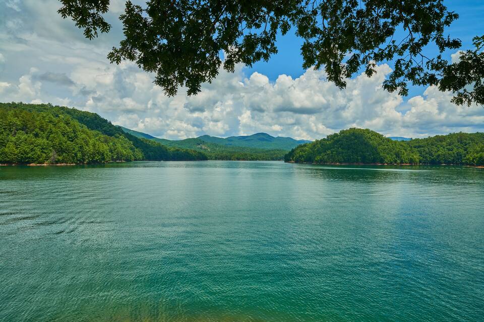 A calm lake surrounded by lush green hills and a partly cloudy sky.