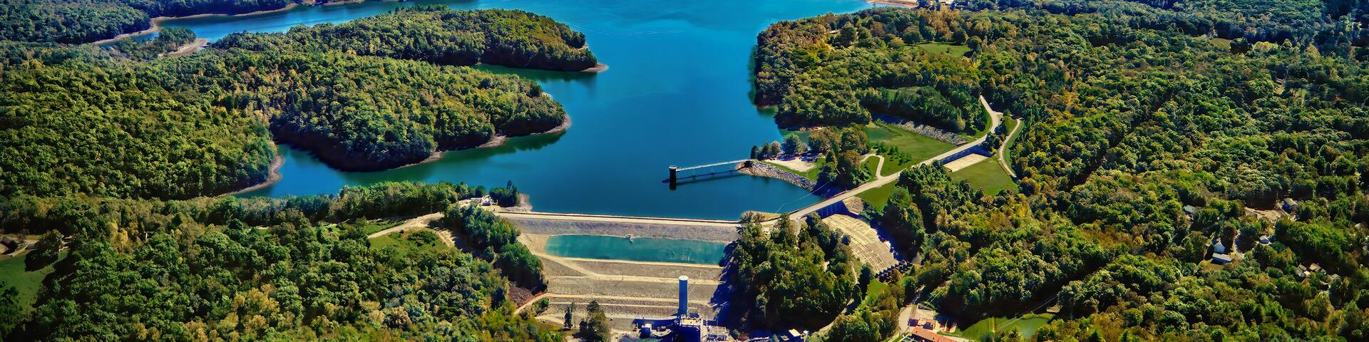 Un lago grande rodeado de colinas boscosas, una represa y un muelle pequeño.