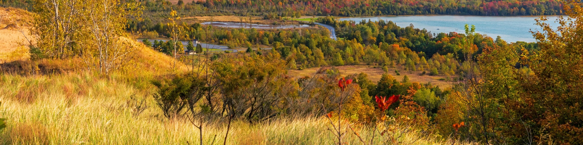 A river winding through a hilly landscape with autumn foliage, a distant body of water, and a small white building.