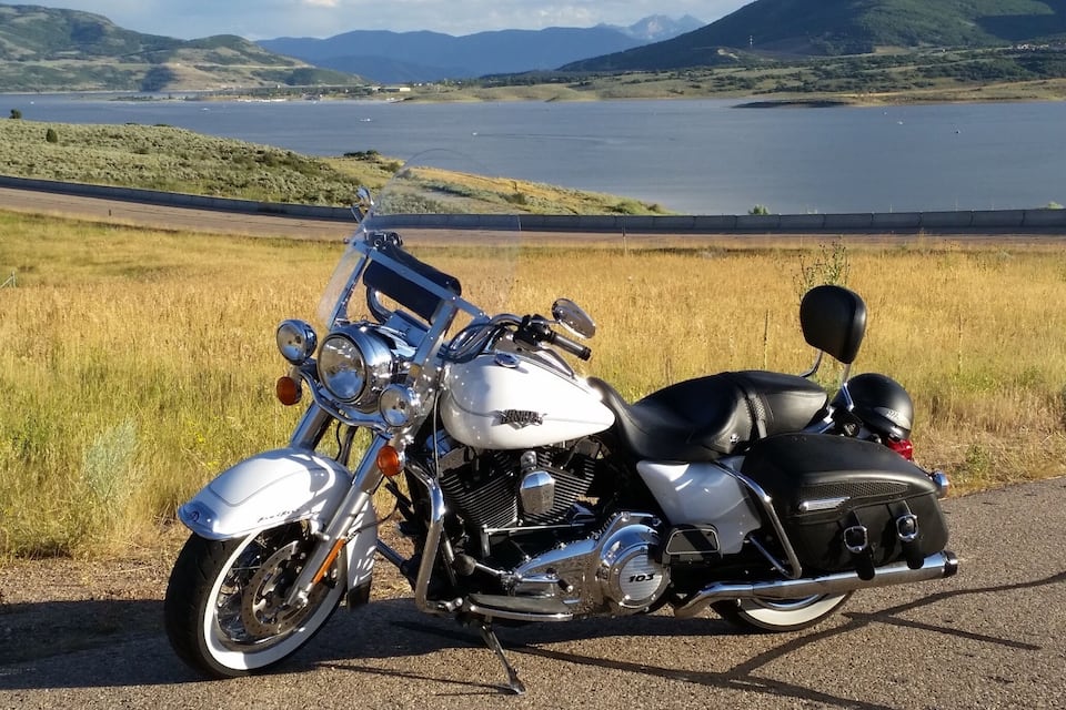 A motorcycle parked by a road with a lake and mountains in the background.