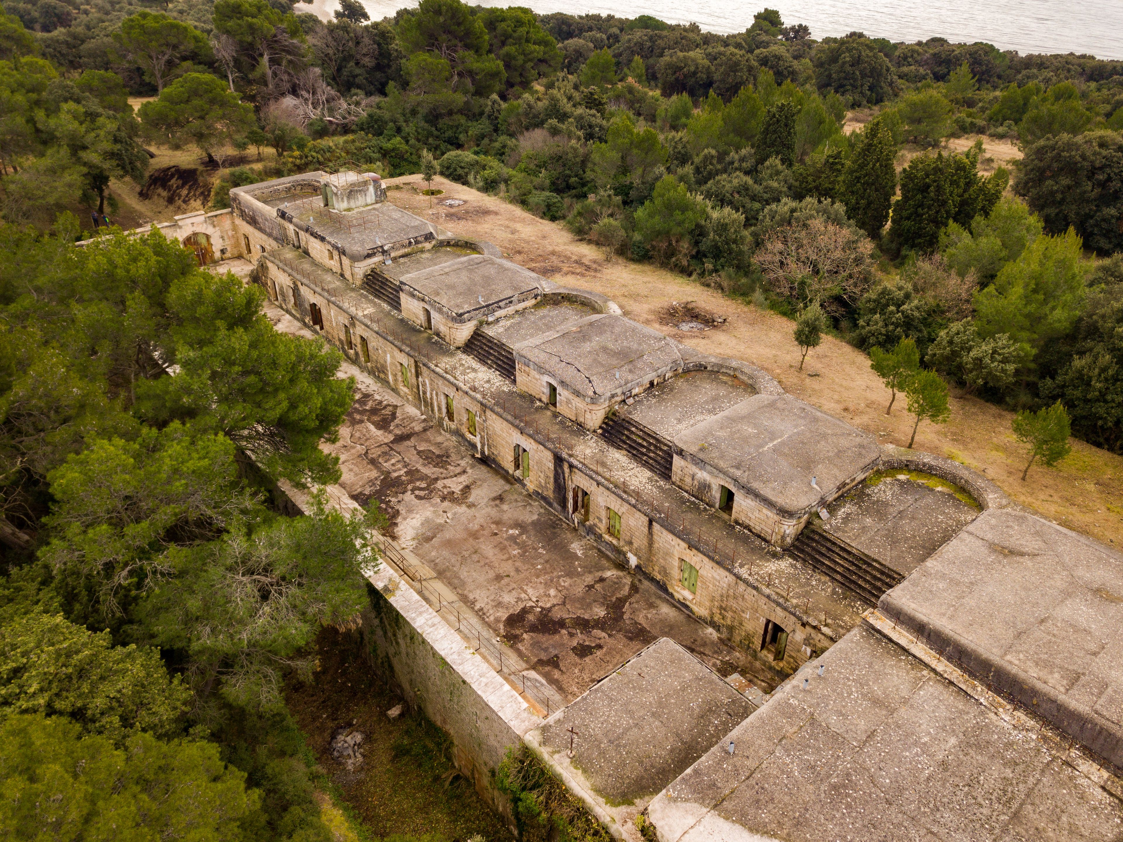 Vue aérienne d’un ensemble de bâtiments historiques entouré d’une végétation luxuriante et d’arbres.
