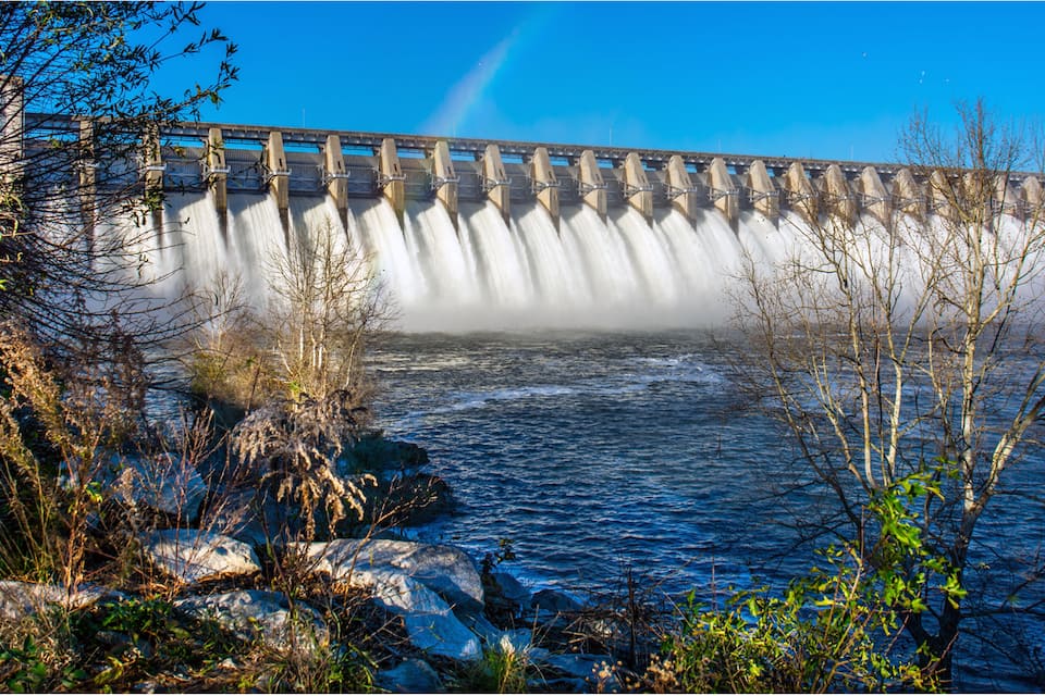 A dam with water flowing over it, surrounded by rocks and vegetation.
