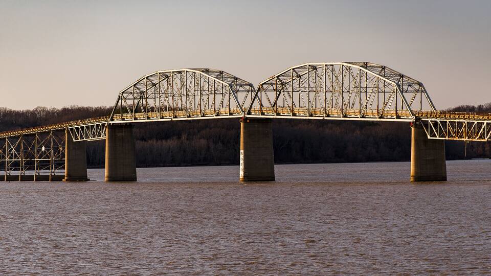 A steel truss bridge over a river with a forest in the background.