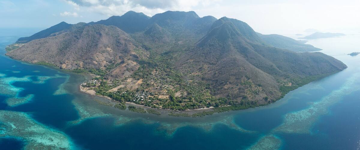 An aerial view of a mountainous island with clear blue waters and a small settlement.
