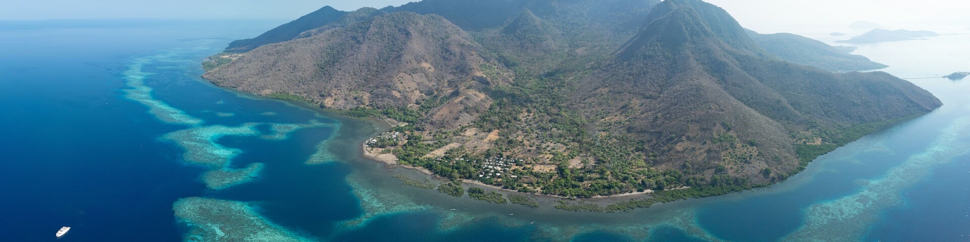 An aerial view of a mountainous island with clear blue waters and a small settlement.