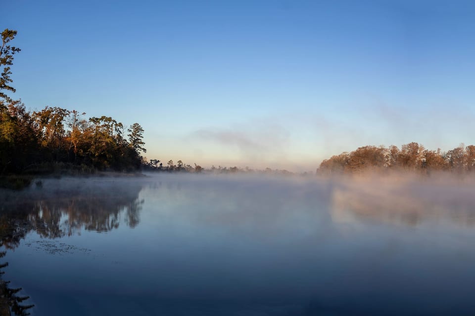 A calm lake with mist and trees reflecting on the water.