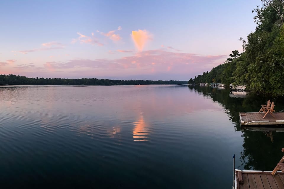 A calm lake at sunset with a dock and trees on the right.