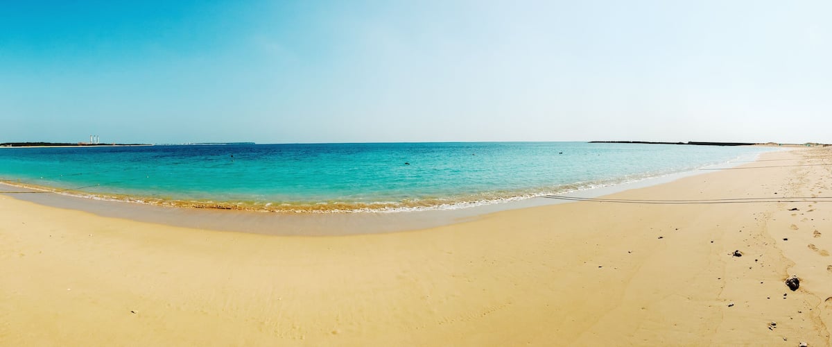 A sandy beach with clear turquoise water and a distant shoreline.