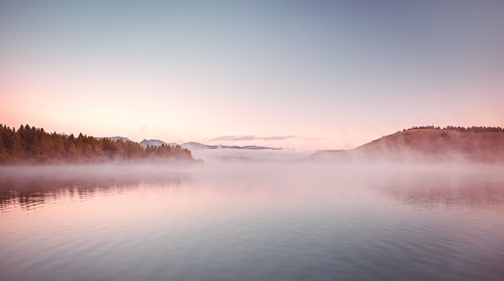 Un lago tranquilo con una orilla boscosa y montañas distantes.