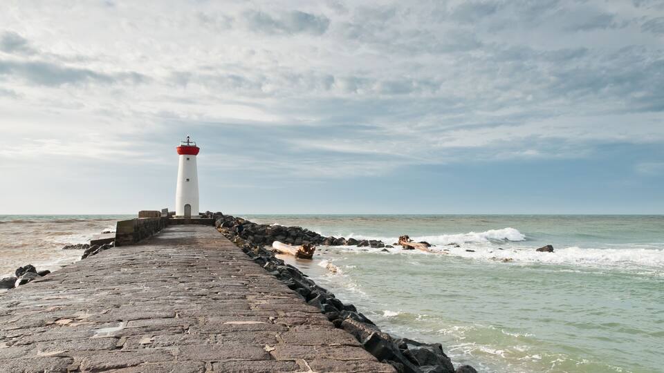 A lighthouse on a stone pier extending into the sea.