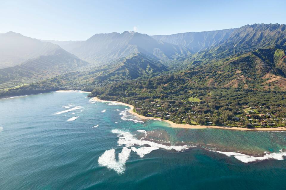 A coastal landscape with mountains, a beach, and clear waters.
