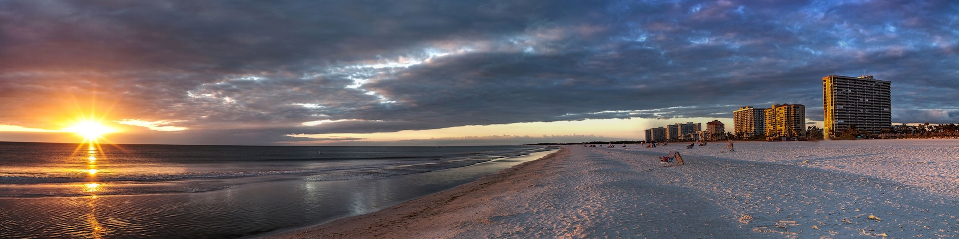 Ein Strand bei Sonnenuntergang, mit Wellen und Hochhäusern im Hintergrund.