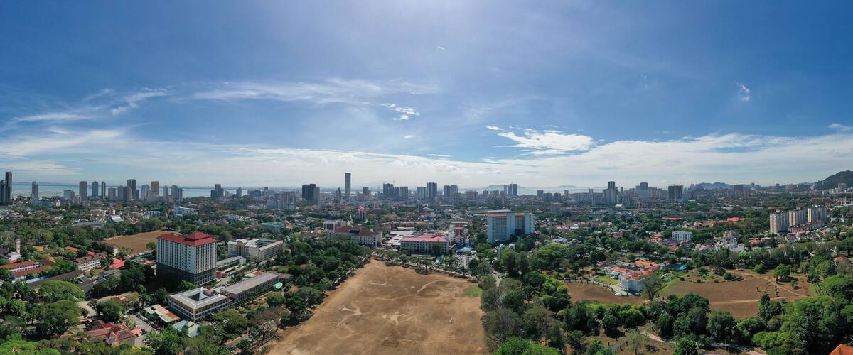 A cityscape with a mix of residential and commercial buildings, a large open field, and a clear blue sky.