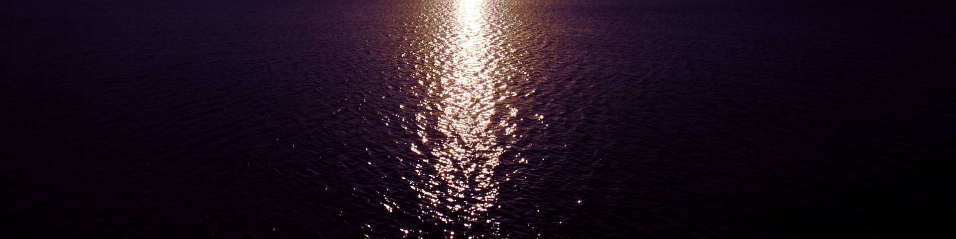 Breathtaking view of a bright sun shining over a dark sea under a cloudy purple sky at sunrise