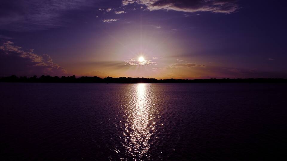 A sunset over a calm body of water with a silhouette of a distant shoreline.
