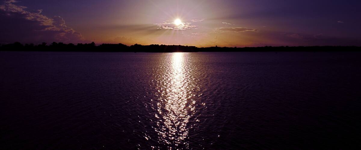 A sunset over a calm body of water with a silhouette of a distant shoreline.
