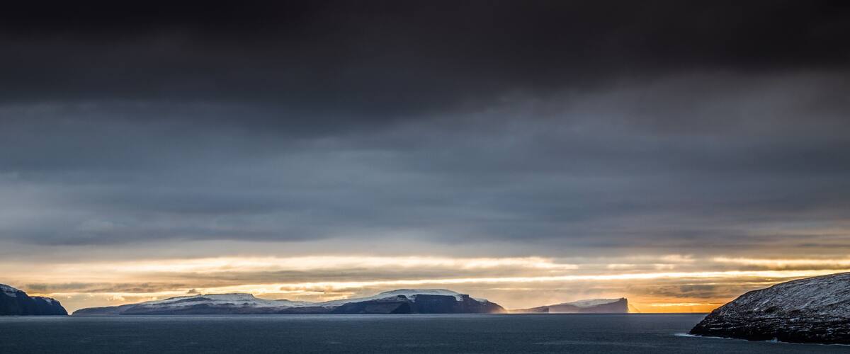 A rugged coastline with snow-covered cliffs and a dramatic sunset over the ocean.