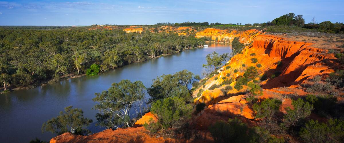 A river winding through a red rock landscape with green vegetation and trees.