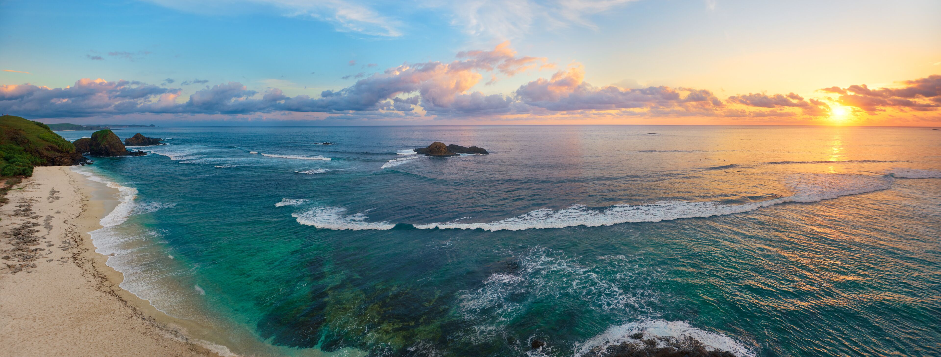 Panoramic view of tropical beach with surfers at sunset.