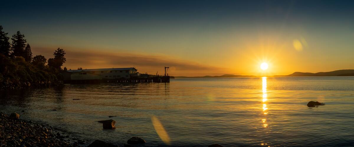 A sunset over a calm lake with a pier and a building on the left.