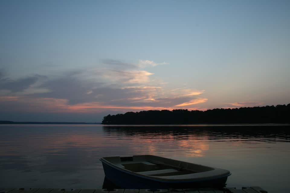 A boat on a calm lake at dusk with a sunset and a forested island in the background.