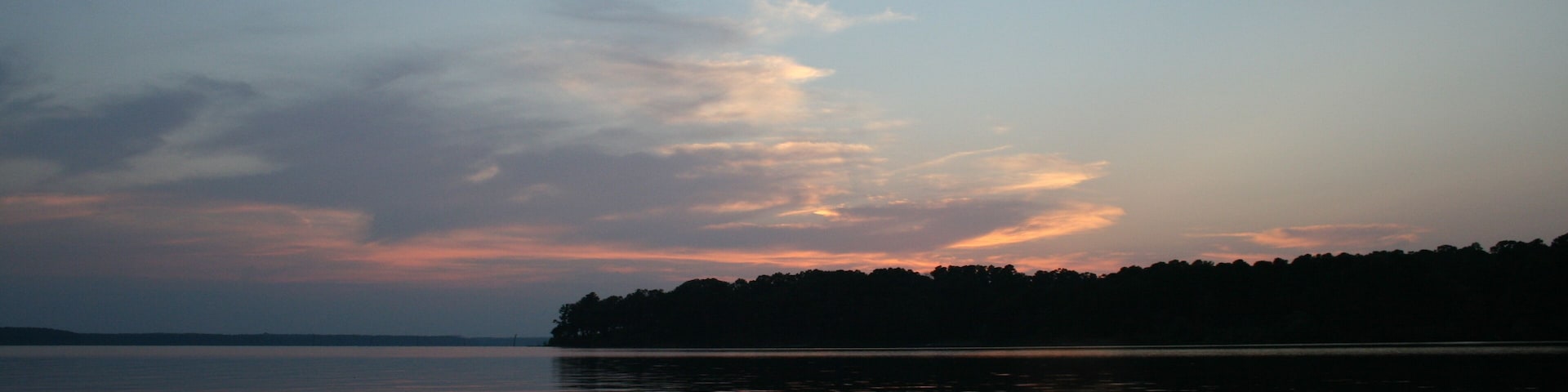 A boat on a calm lake at dusk with a sunset and a forested island in the background.