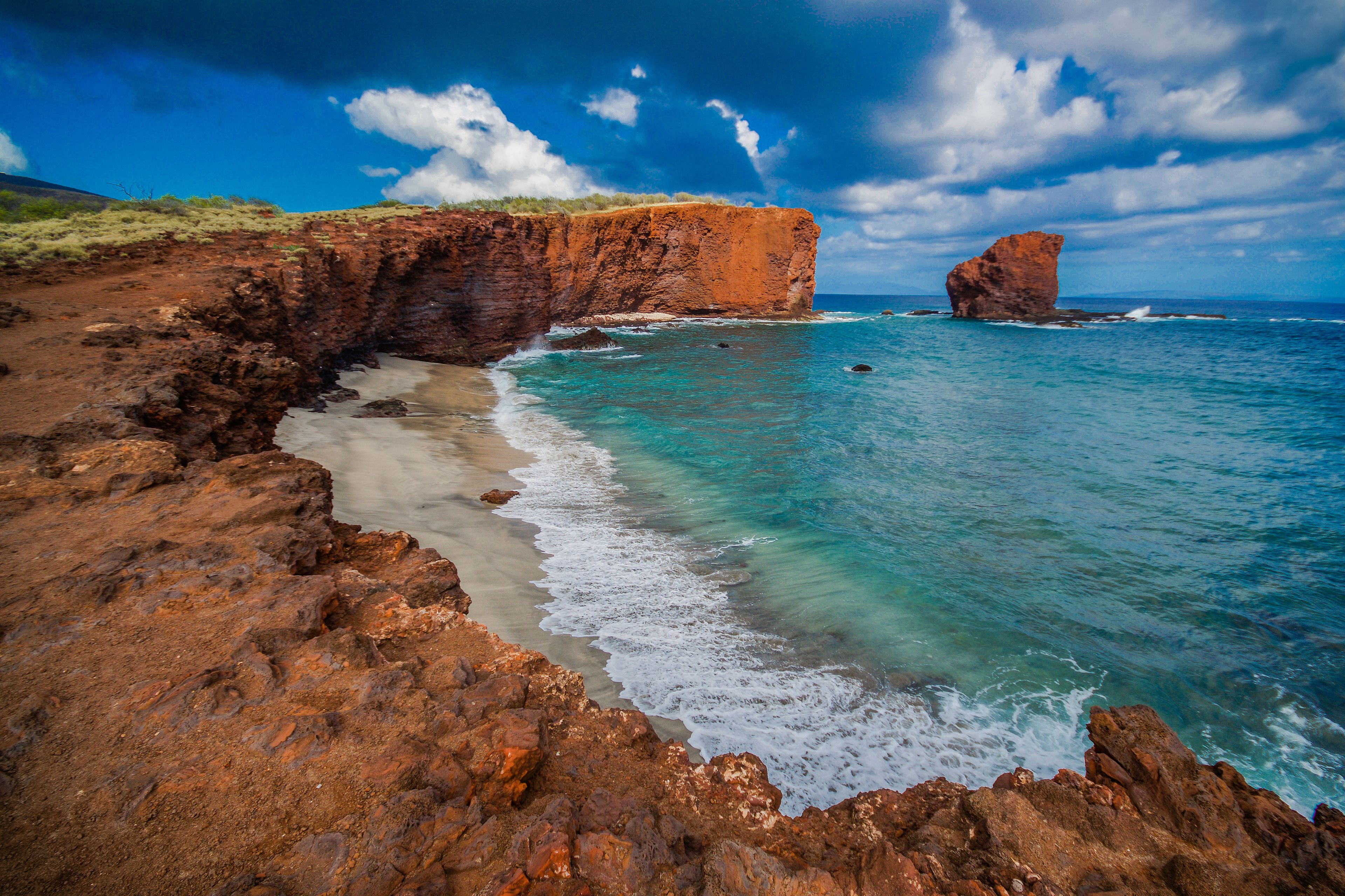 A coastal landscape with red cliffs, clear turquoise waters, and a sandy beach.