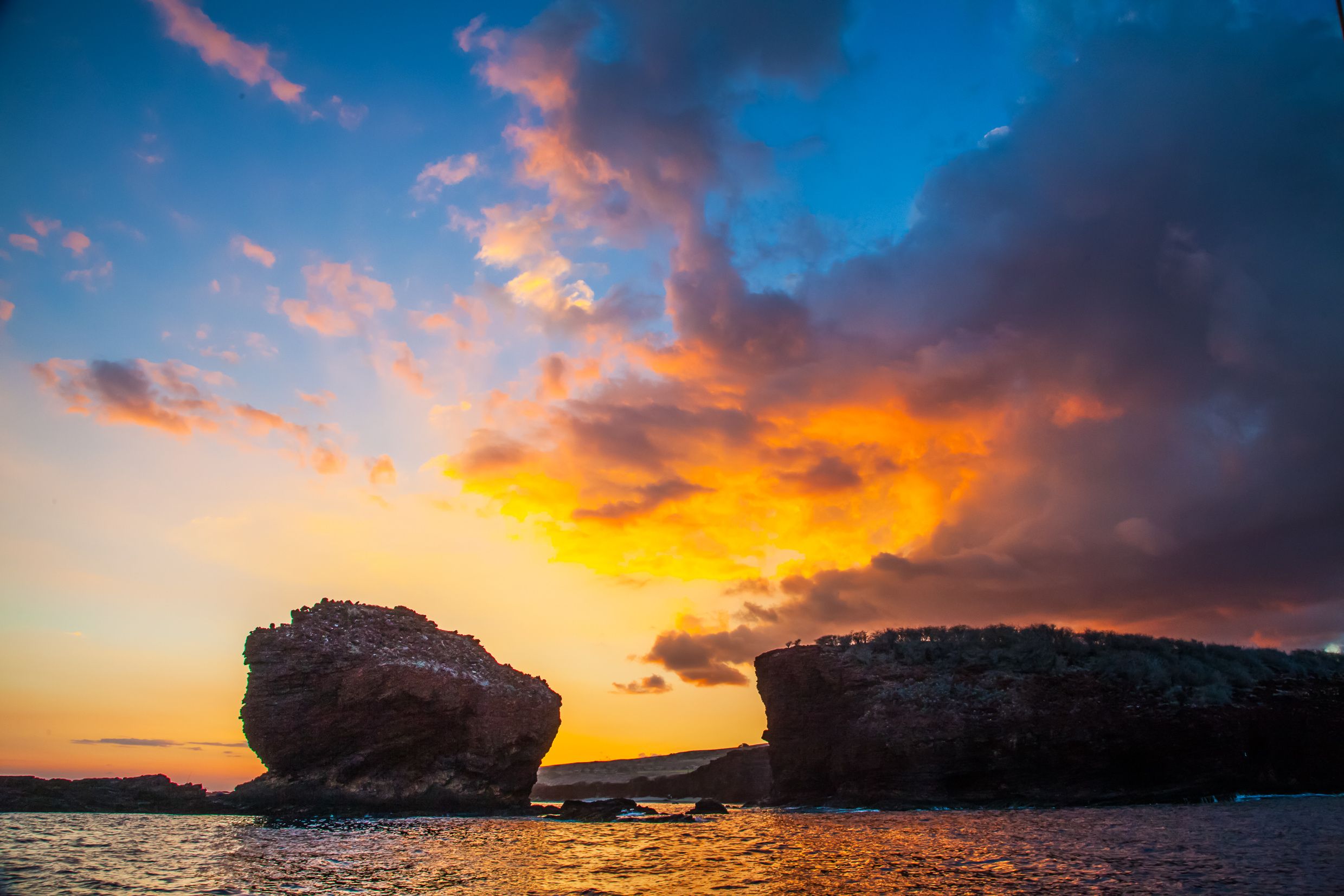 Un coucher de soleil sur un paysage côtier, avec deux formations rocheuses particulièrement imposantes.