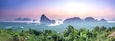 A mountainous landscape with a sunrise or sunset, featuring prominent rock formations and lush greenery.