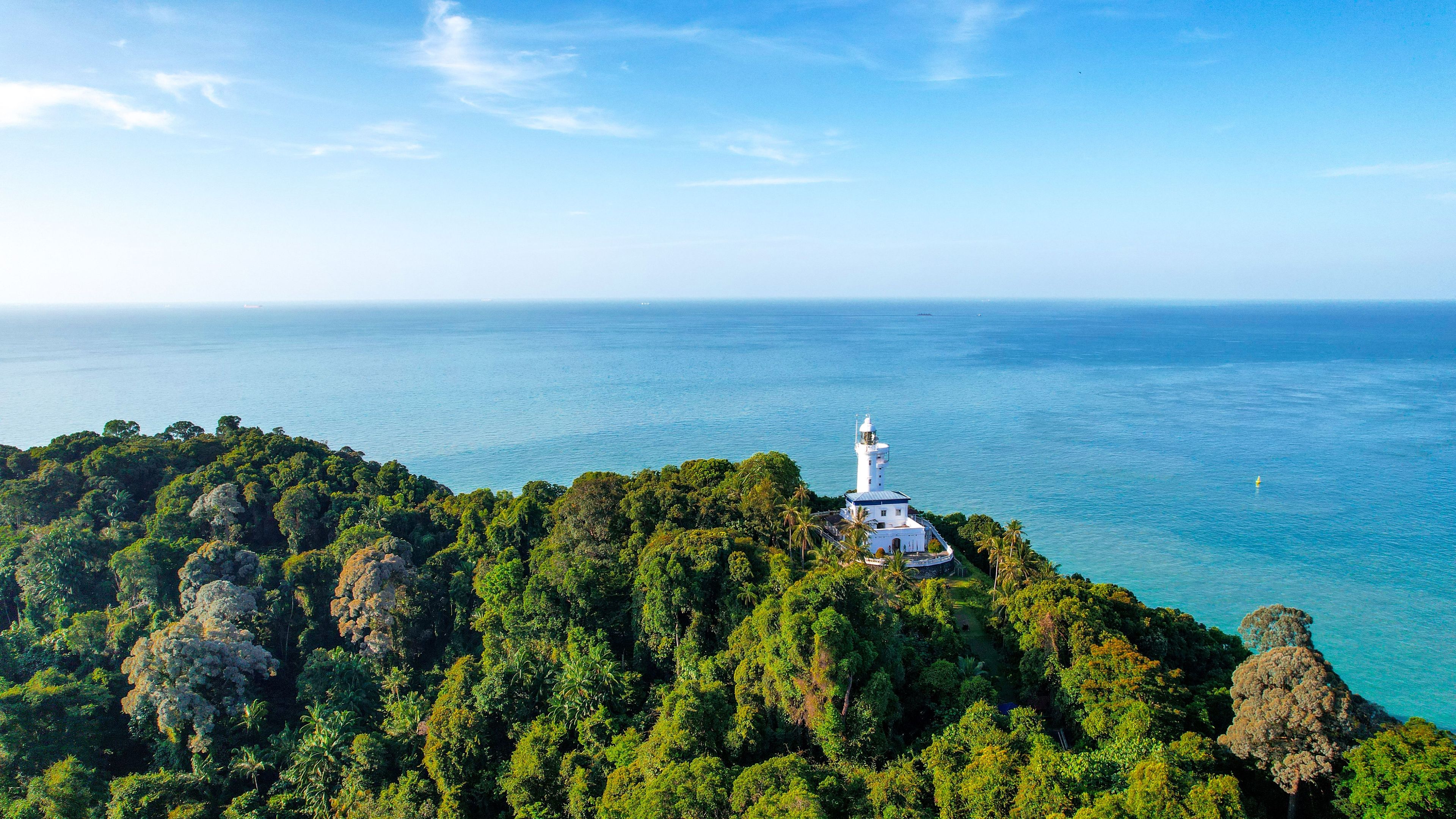 A white lighthouse on a lush green island surrounded by clear blue waters.