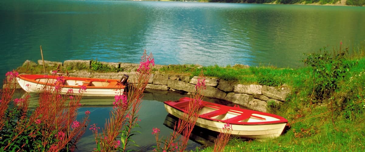 A lake surrounded by mountains with two boats docked at a stone pier.