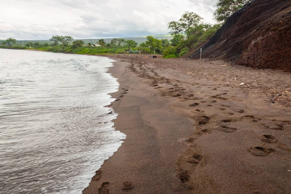 A beach with footprints in the sand, a cliff, and a cloudy sky.