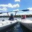 Two people kayaking on a calm lake with trees in the background.