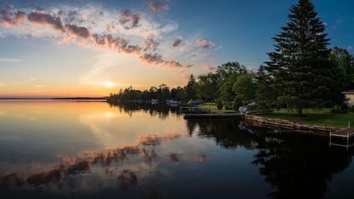 A calm lake at sunset with a dock and trees reflecting the sky.