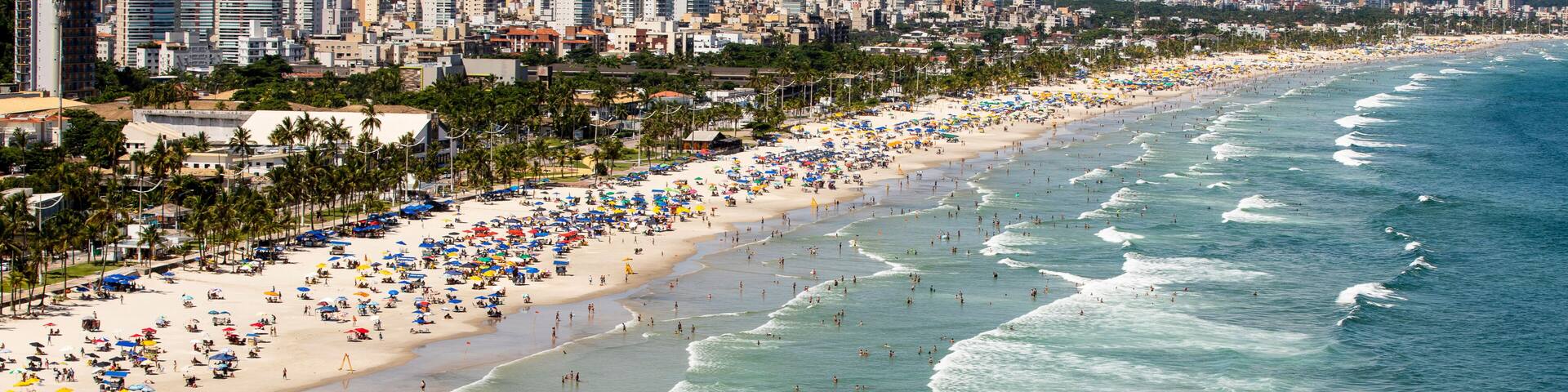 A coastal cityscape with a wide beach, numerous umbrellas, and a clear view of the ocean.