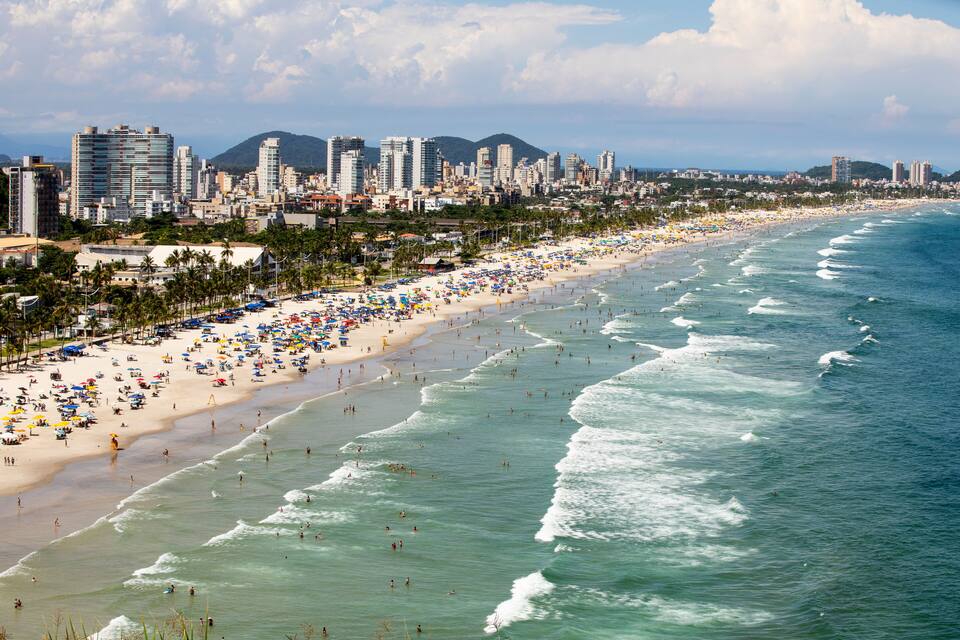 A coastal cityscape with a wide beach, numerous umbrellas, and a clear view of the ocean.