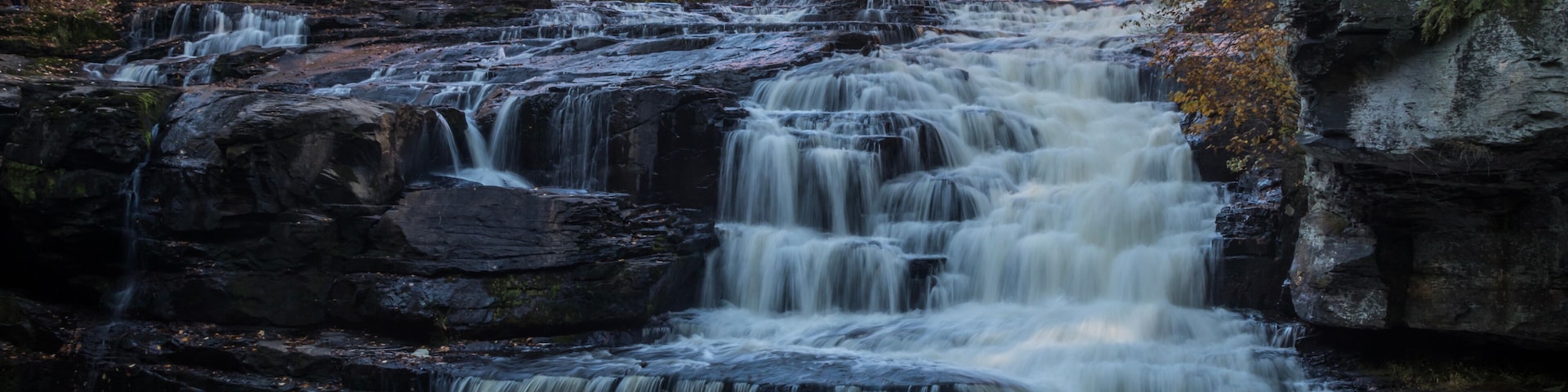 Una cascada en varios niveles rodeada de árboles de colores otoñales.