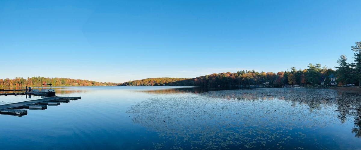 A calm lake with a dock, surrounded by trees and hills.