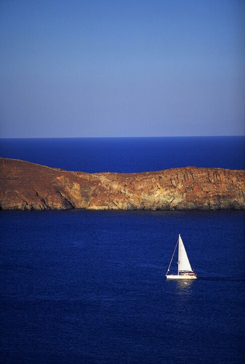 A sailboat on a calm sea with a rocky coastline in the background.