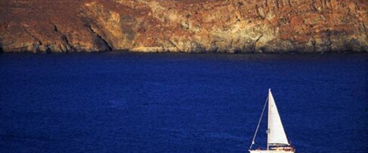 A sailboat on a calm sea with a rocky coastline in the background.