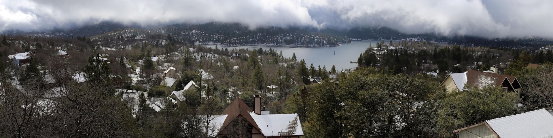 A mountainous landscape with a lake, houses, and dense forest.